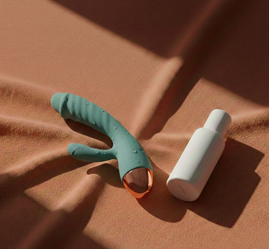 A minimalist arrangement of a blue vibrator and a white skincare bottle on a terracotta linen surface with soft shadows.