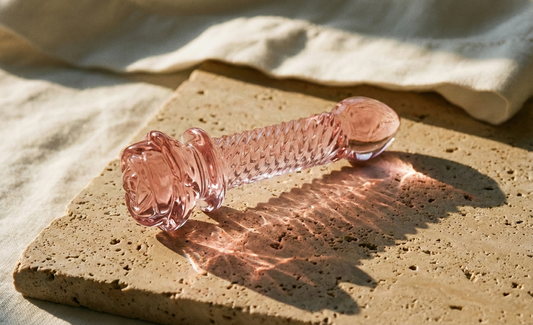 The Rosé, a Pink glass pipe on a textured surface with a beige cloth in the background
